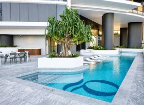 A modern indoor pool area with a large tree, seating, and a clear pool edge. - New Apt in Queens Wharf lv21 with Sofa bed (Brisbane City)