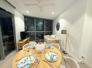 A modern living room with a round dining table set for four, a sofa, a TV, and a large window. - New Apt in Queens Wharf lv21 with Sofa bed (Brisbane City)