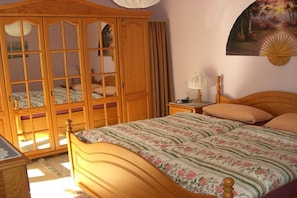 A bedroom with a wooden bed, a nightstand, a wooden wardrobe, and a painting on the wall. - Sauer with lake and alpine views (Immenstaad am Bodensee)