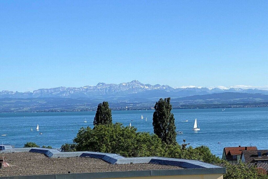 Un lac où voguent des voiliers, avec des montagnes en arrière-plan et des arbres au premier plan.