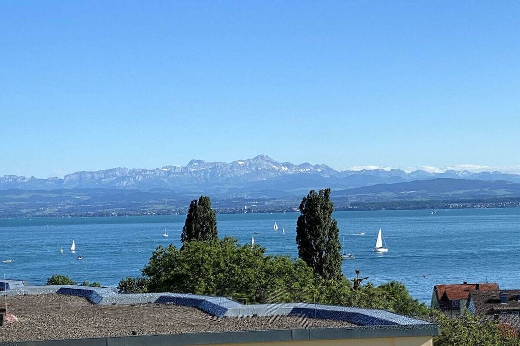 A lake with sailboats, mountains in the background, and trees in the foreground.