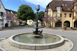 A public square with a central fountain, surrounded by buildings and trees. - Sauer with lake and alpine views (Immenstaad am Bodensee)