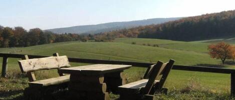 A picnic table and benches in a natural setting with a view of a green field and distant hills.