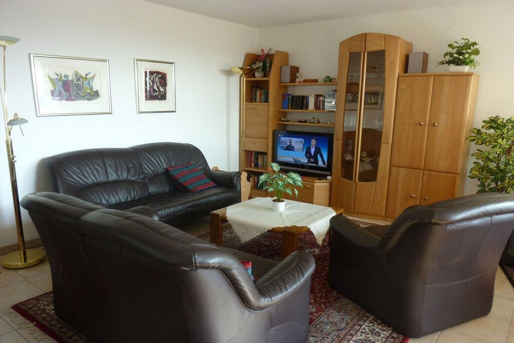 A living room with a black leather sofa, a television, a wooden cabinet, and a floor lamp.