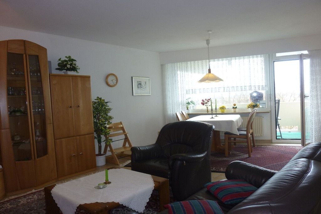 A living room with a leather sofa, a wooden cabinet, a dining table with chairs, and a window with curtains.