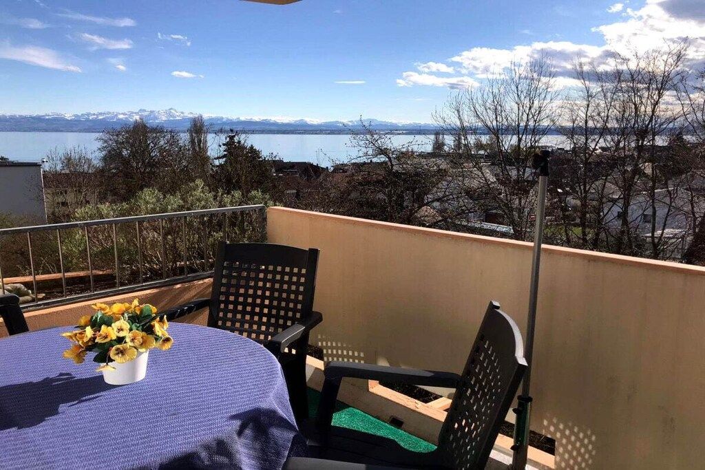 A balcony with a table and chairs, a vase of flowers, and a view of a lake and mountains.
