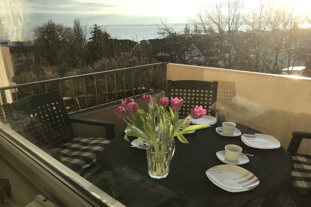 Un balcon avec une table dressée pour deux personnes, un vase rempli de fleurs et une vue sur la mer.