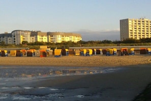 Um hotel à beira-mar com vários edifícios, uma praia de areia e uma fileira de cabanas de praia.