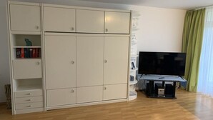 A room with a large white wardrobe, a flat-screen TV on a stand, and a green curtain. - Döse beach high-rise (Cuxhaven)