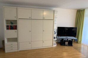 Quarto com um guarda-roupa branco grande, uma TV de tela plana em um suporte e uma cortina verde.