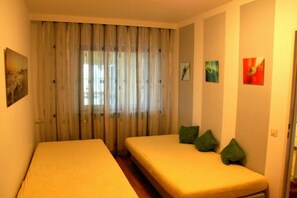 Habitació amb dos llits individuals, una finestra amb cortines fines i una obra d'art a la paret.
