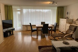 Sala de estar com televisão, mesa de jantar, cadeiras e sofá.