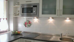 A kitchen with white cabinets, a stainless steel sink, a microwave, and a fruit bowl on the counter. - Döse beach high-rise (Cuxhaven)