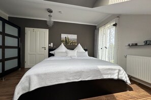 A bedroom with a large bed, a door, a window with curtains, and a radiator. - Holiday apartment with 1 bedroom (Rüdesheim am Rhein)