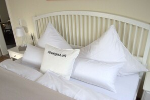 Ein Bett mit weißer Bettwäsche und Kissen, ein Nachttisch mit einer Lampe und ein weißes Kopfende.