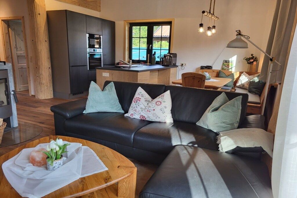Een moderne woonkamer met een zwarte leren bank, een houten salontafel en een keukenhoek met een inbouwoven en spoelbak.