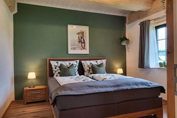 Ein Schlafzimmer mit einem Bett, zwei Nachttischen, einer Wandlampe und einem Fenster mit Vorhängen.
