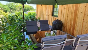Ein überdachter Außenbereich mit einer Holzverkleidung, zwei Stühlen, einem Tisch und einem Grill.