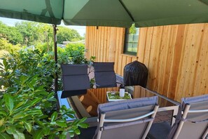 A covered outdoor seating area with a wooden wall, two chairs, a table, and a grill. - Raccoon Hut Steirer-Hof (Vöhl)