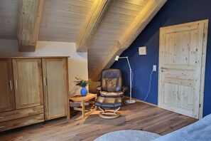 A room with wooden flooring, a leather chair, a desk with a plant, and a wardrobe. - Raccoon Hut Steirer-Hof (Vöhl)