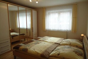 Quarto com duas camas, um guarda-roupa e uma janela com cortinas.
