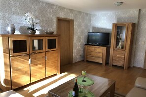Ein Wohnzimmer mit Holzsäcken, einem Fernseher und einem grünen Tisch mit einer Flasche und einem Glas.