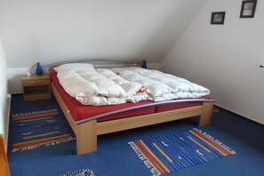 Ein Schlafzimmer mit einem Bett, einem Nachttisch, einem blau-roten Teppich und einer Wand mit zwei gerahmten Bildern.