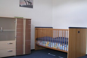 A room with a wooden crib, a wardrobe with multiple drawers, and a painting on the wall. - Holiday home with 3 bedrooms (Wietzendorf)