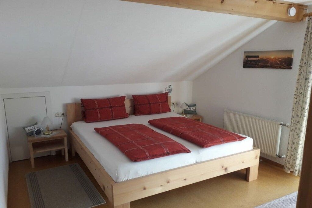Ein Einzelbett mit Holzrahmen, weißer Bettwäsche und roten Kissen in einem Zimmer mit schrägen Decken und einer Heizung.