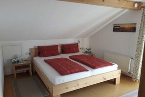 Ein Einzelbett mit Holzrahmen, weißer Bettwäsche und roten Kissen in einem Zimmer mit schrägen Decken und einer Heizung.