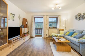 A well-lit living room with a television, wooden furniture, a sofa, and a view of the outdoors through a window.