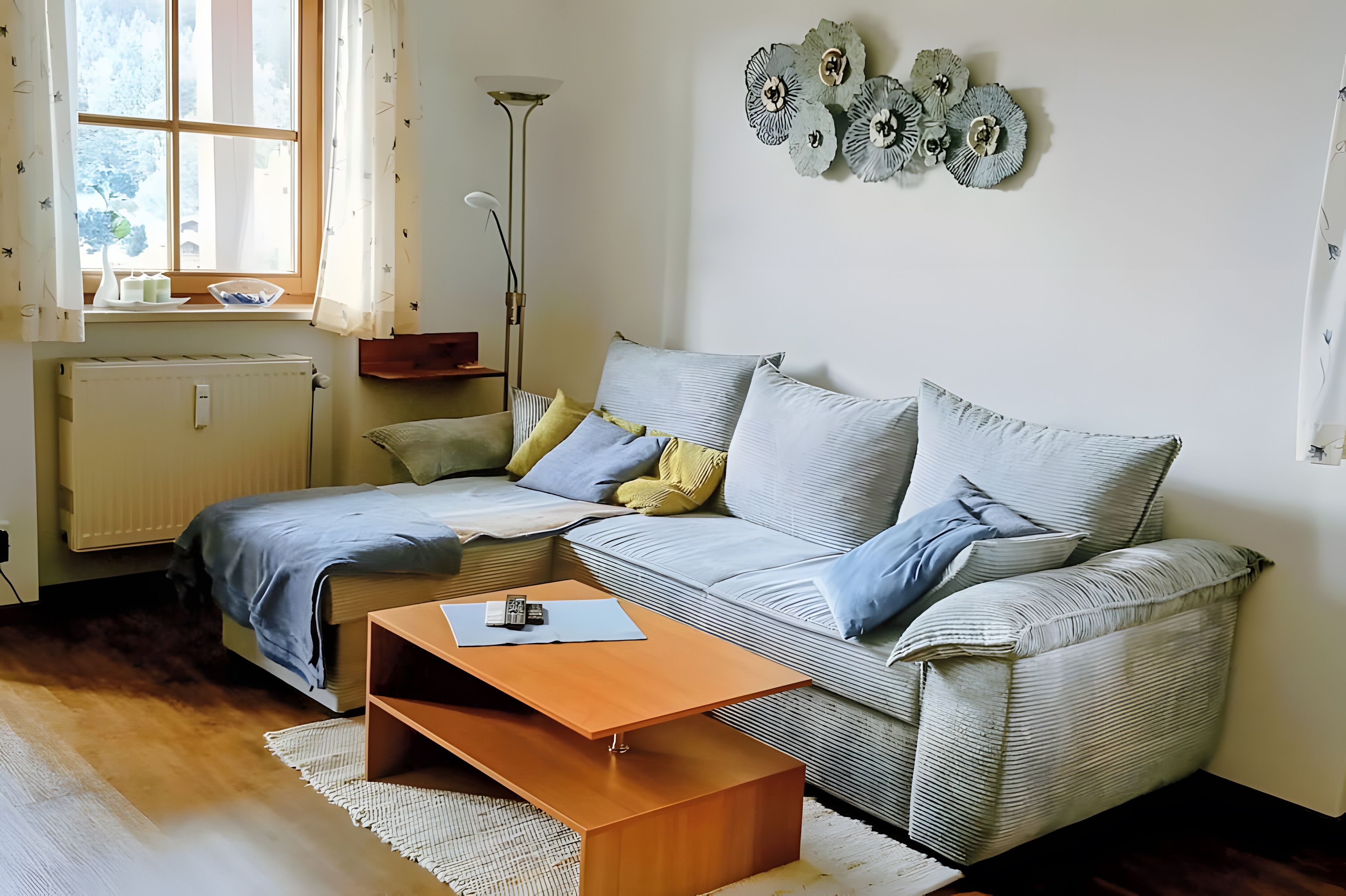 Un salon comprenant un canapé, une table basse, un radiateur, une fenêtre avec des rideaux et des éléments de décoration murale.