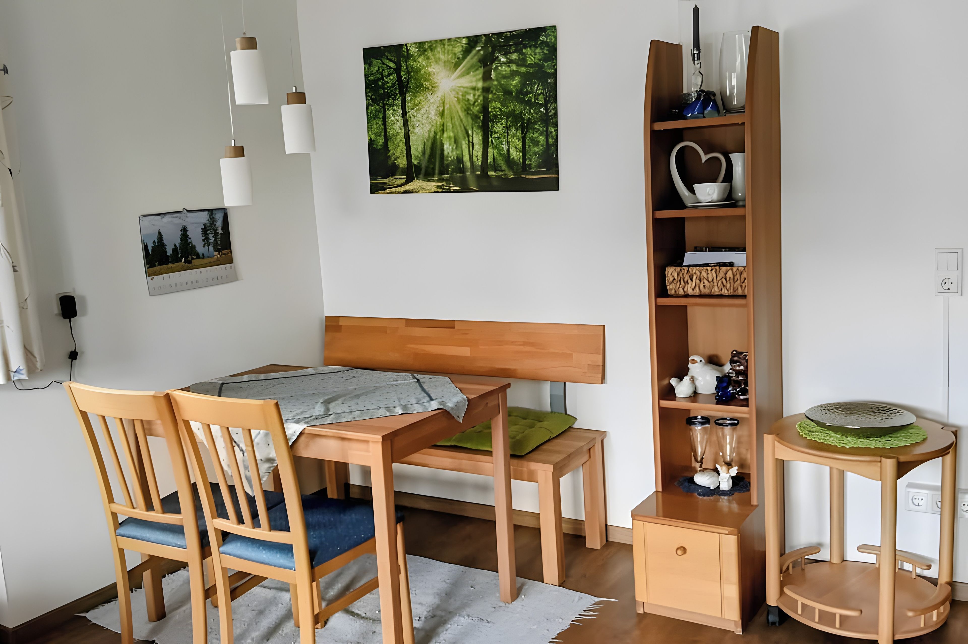 Une pièce comprenant un lit en bois, un bureau avec une chaise, une bibliothèque et une petite table surmontée d’un tapis vert.