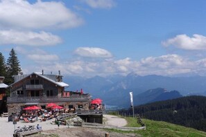 Eine Berghütte mit Sitzgelegenheiten im Freien und Blick auf die Berge.