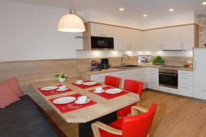 Eine moderne Küche mit weißen Schränken, einem Esstisch für vier Personen und einem eingebauten Backofen.