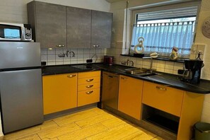 A kitchen with a refrigerator, microwave, and a window with blinds. - Holiday home with 2 bedrooms (Tossens\/Butjadingen)