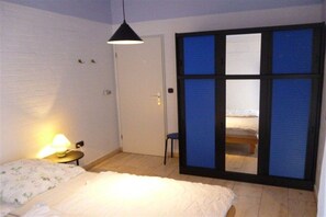 A bedroom with a bed, a chair, a nightstand with a lamp, and a sliding door leading to a balcony. - Holiday home with 2 bedrooms (Tossens\/Butjadingen)