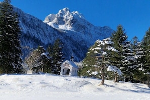 A snow-covered landscape with a small white church, a mountain in the background, and evergreen trees. - Holiday apartment with 1 bedroom (Garmisch-Partenkirchen)