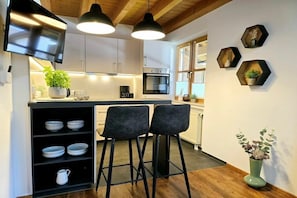 A modern kitchen with a central island, bar stools, a TV mounted on the wall, and hexagonal wall shelves. - Holiday apartment with 1 bedroom (Garmisch-Partenkirchen)