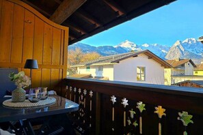 A balcony with a view of snow-capped mountains, wooden railings, and a table with a vase and glasses. - Holiday apartment with 1 bedroom (Garmisch-Partenkirchen)