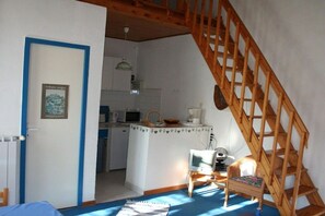Quarto com escada de madeira, cozinha e uma pequena mesa com cadeira.