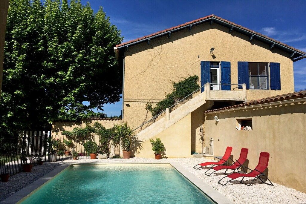 A poolside area with a pool, red lounge chairs, and a building with blue shutters.