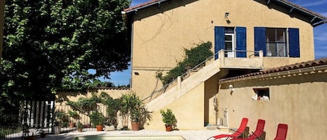 A poolside area with a pool, red lounge chairs, and a building with blue shutters.