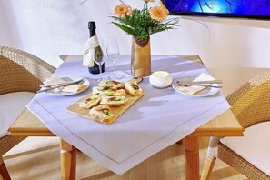 Une table dressée pour deux personnes, avec une nappe blanche, une bouteille de champagne, un vase rempli de fleurs et une assiette de hors-d'œuvre.