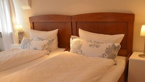 Uma cama de casal com cabeceira de madeira, duas mesas de cabeceira com abajures e almofadas estampadas.