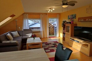 Ein Wohnzimmer mit Sofa, Couchtisch, Fernseher und einer Treppe, die in einen Außenbereich führt.