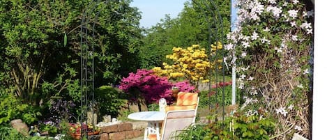 A garden with a metal archway, a table with chairs, and various flowering plants.