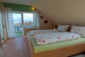 Ein Schlafzimmer mit einem Bett, einem Fenster mit Vorhängen und Blick auf einen Balkon.
