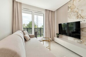 A modern living room with a sofa, a TV mounted on the wall, and a balcony with curtains. - Air-conditioned Apartment with a View of the Water | Close to the City Centre (Gdańsk)