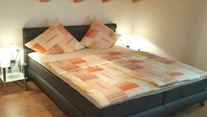 A bed with a patterned bedspread, two pillows, a bedside table with a lamp, and a wooden ceiling structure. - Holiday apartment with 1 bedroom (Oberammergau)